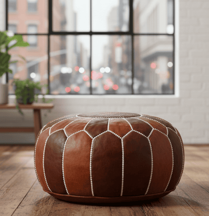 Brown leather ottoman on a wooden floor with a cityscape view through a window.