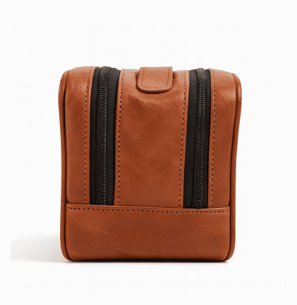 Brown leather toiletry bag with black zippers on a white background